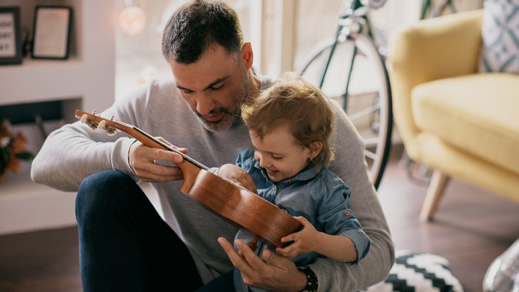 Father showing to his daughter what ukulele is